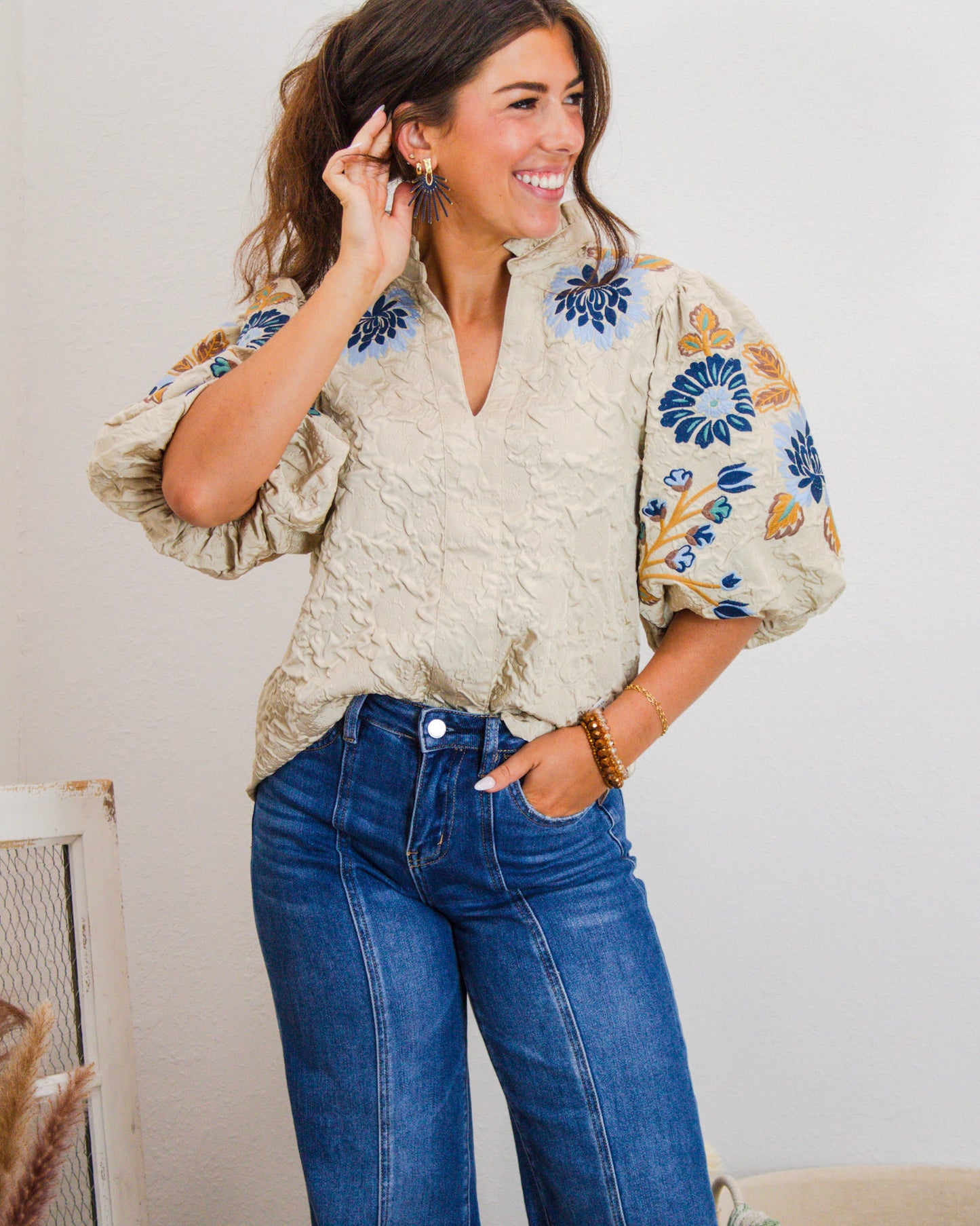 Woman wearing a beige embroidered puff sleeve blouse with blue and mustard floral details, paired with high-rise wide-leg jeans.