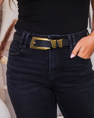Close-up of a woman wearing high-waisted black denim jeans paired with a wide black belt featuring a vintage-style brass buckle and a fitted black tank top.