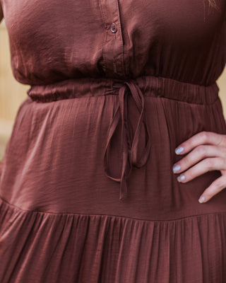 Close-up of a brown satin midi dress with a drawstring waist and tiered skirt, showcasing the soft texture and flattering feminine silhouette.