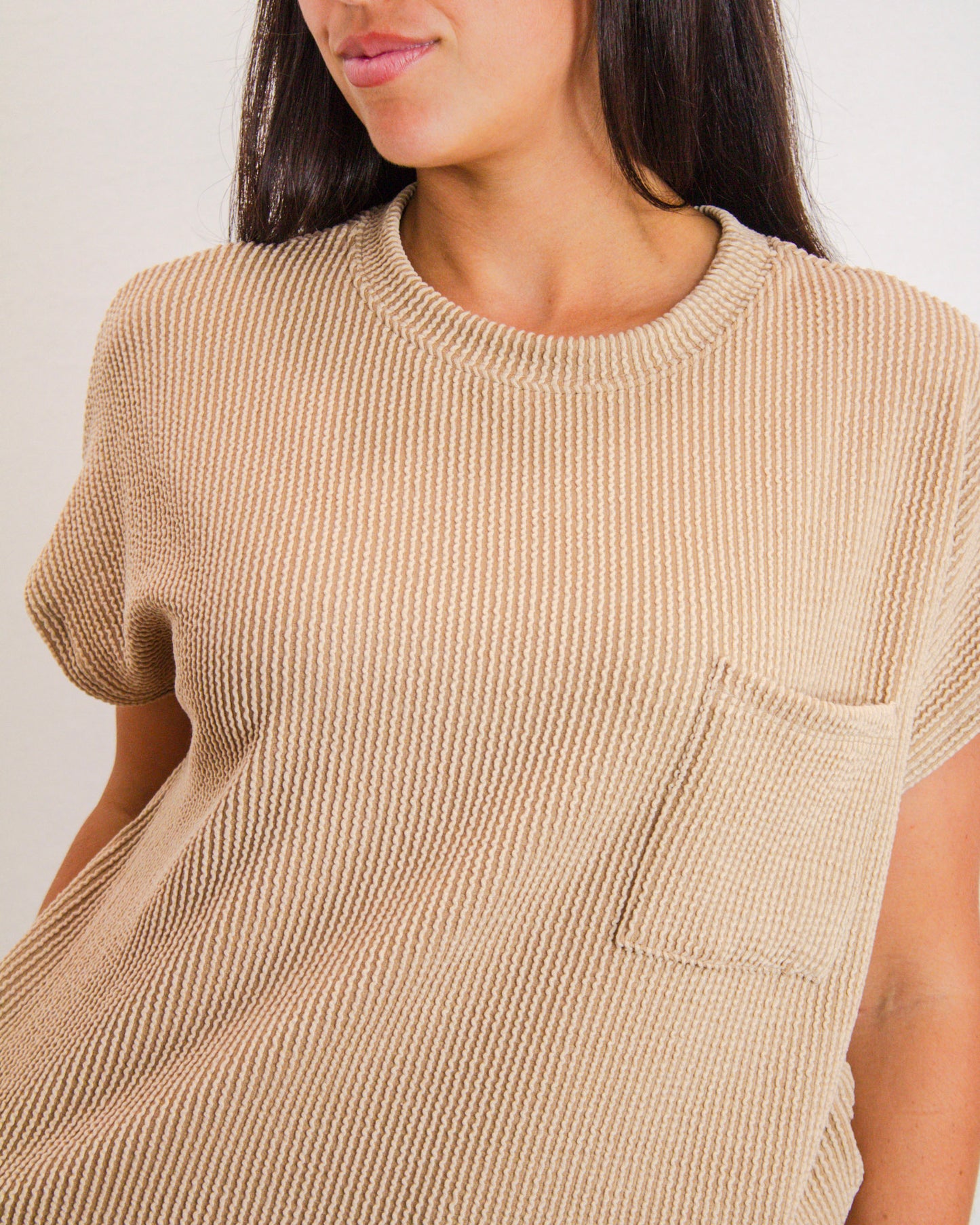 Close-up of woman wearing a beige ribbed short sleeve knit top with front pocket, showcasing cozy texture and casual boutique style.