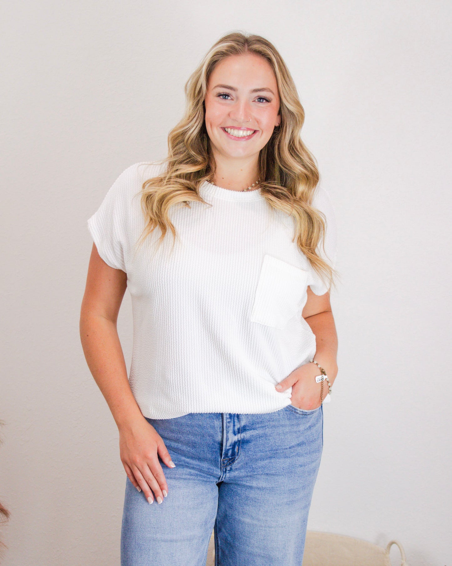 Woman wearing a casual white ribbed short sleeve top with front pocket, paired with high-rise light wash jeans, styled for a boutique fashion look.