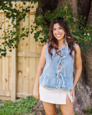 Woman smiling in a light-wash denim peplum top with a tie-front and a cream mini skirt