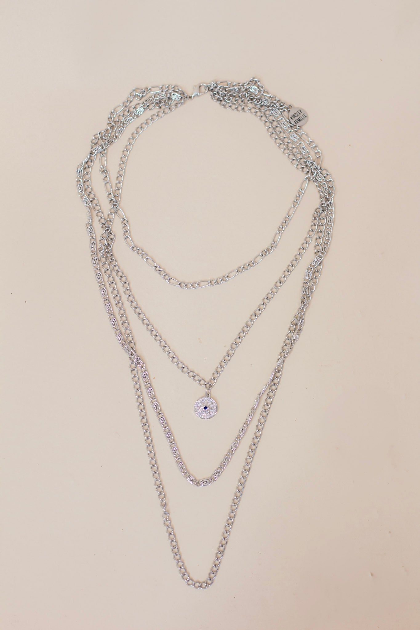 Layered silver chain necklace featuring multiple chain styles and a small pavé evil eye pendant. Trendy multi-chain jewelry for a bold, stacked look.