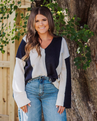 Smiling woman wearing a navy and cream colorblock V-neck sweater with wide sleeves, paired with high-waisted light wash jeans for a cozy fall outfit.