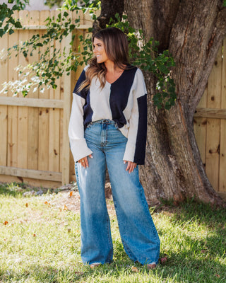 Woman wearing a navy and cream colorblock V-neck sweater paired with high-waisted wide leg light wash jeans, styled outdoors for a casual fall look.