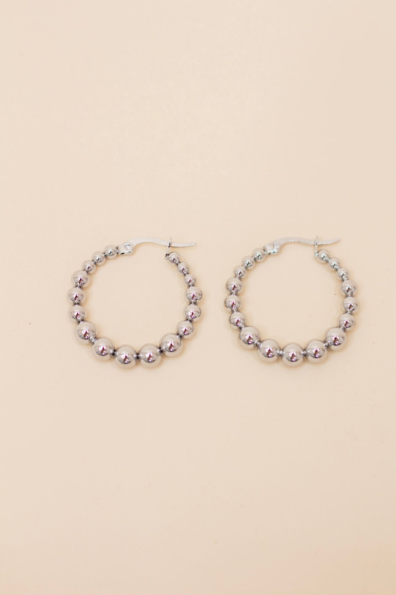 Pair of silver beaded hoop earrings featuring polished metallic round beads and a latch-back closure. Lightweight, trendy jewelry for everyday wear or special occasions.