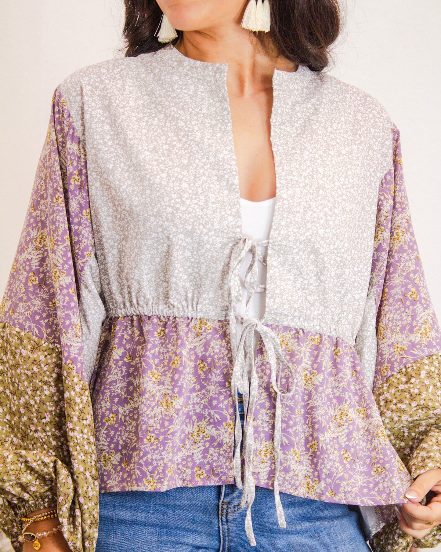 Close-up of a floral patchwork boho blouse with drawstring waist, featuring lavender, green, and cream panels, styled with denim jeans for a boutique look.