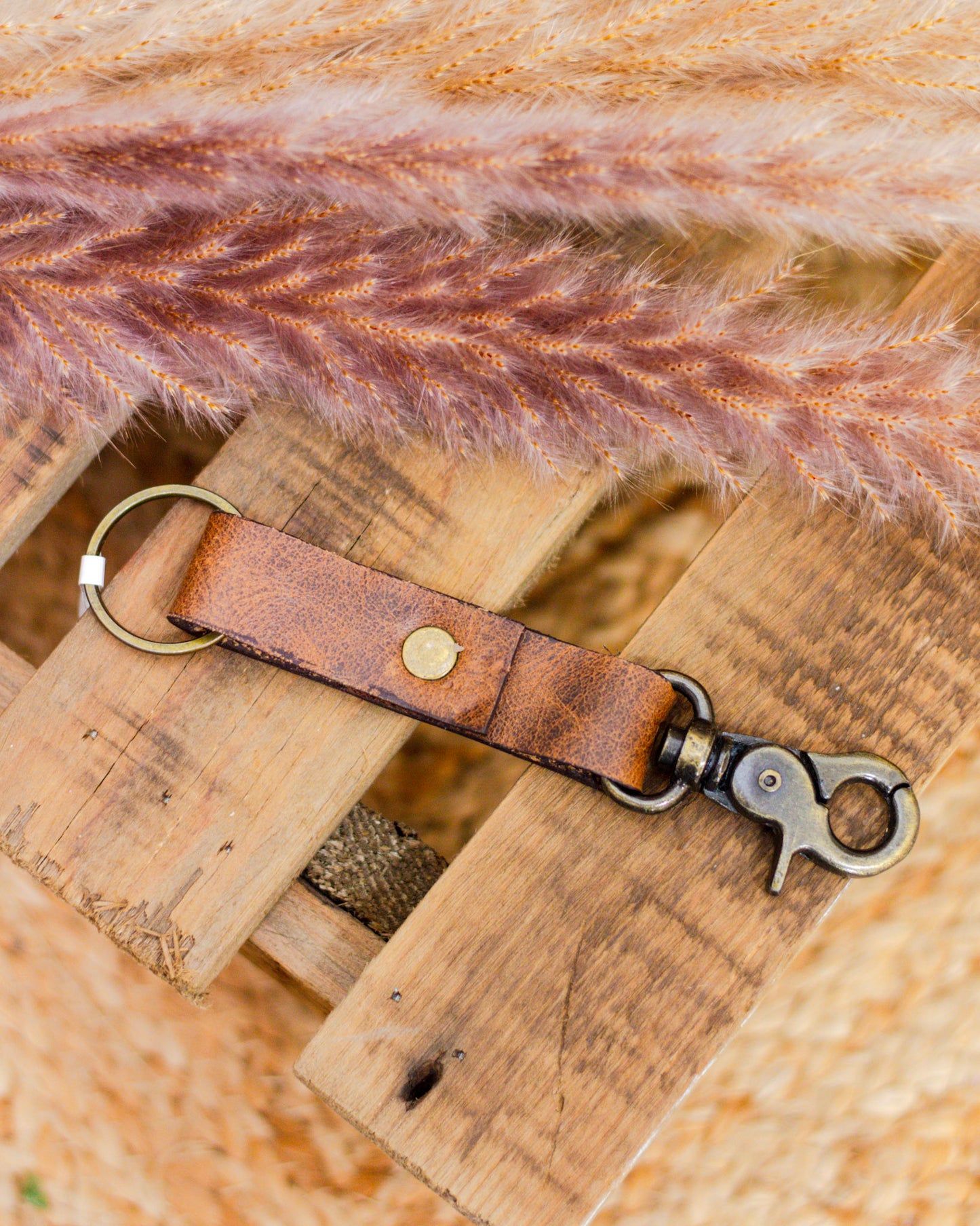 Handcrafted brown leather keychain with brass hardware and swivel clasp on rustic wooden surface – durable and stylish everyday accessory.