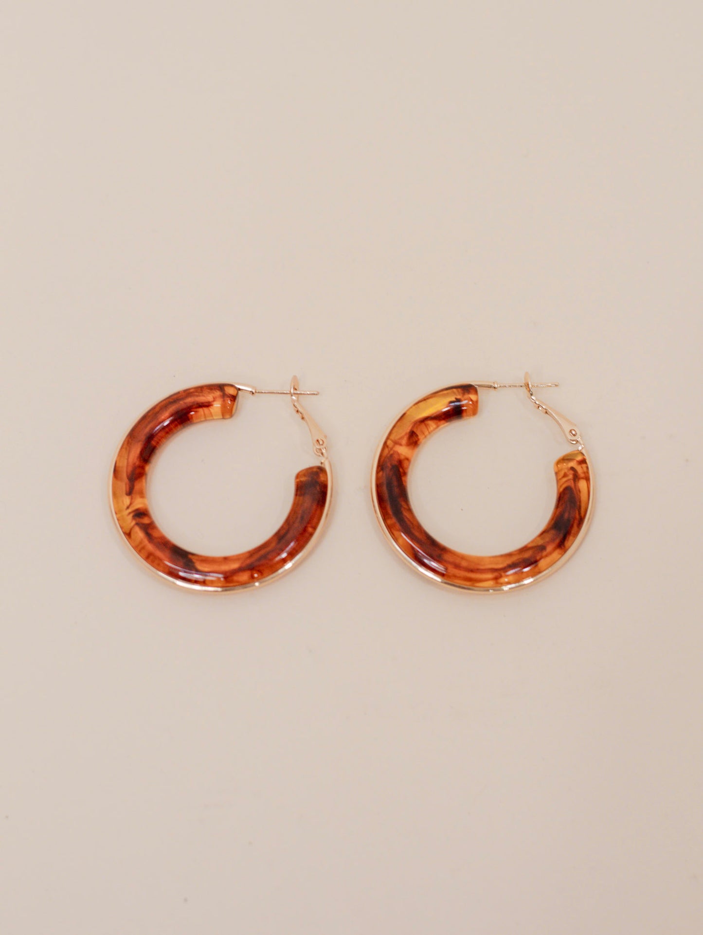 Pair of round hoop earrings with a glossy tortoiseshell pattern in warm brown and amber tones, finished with gold-tone hardware. Bold, retro-inspired statement earrings for everyday or dressy styling.