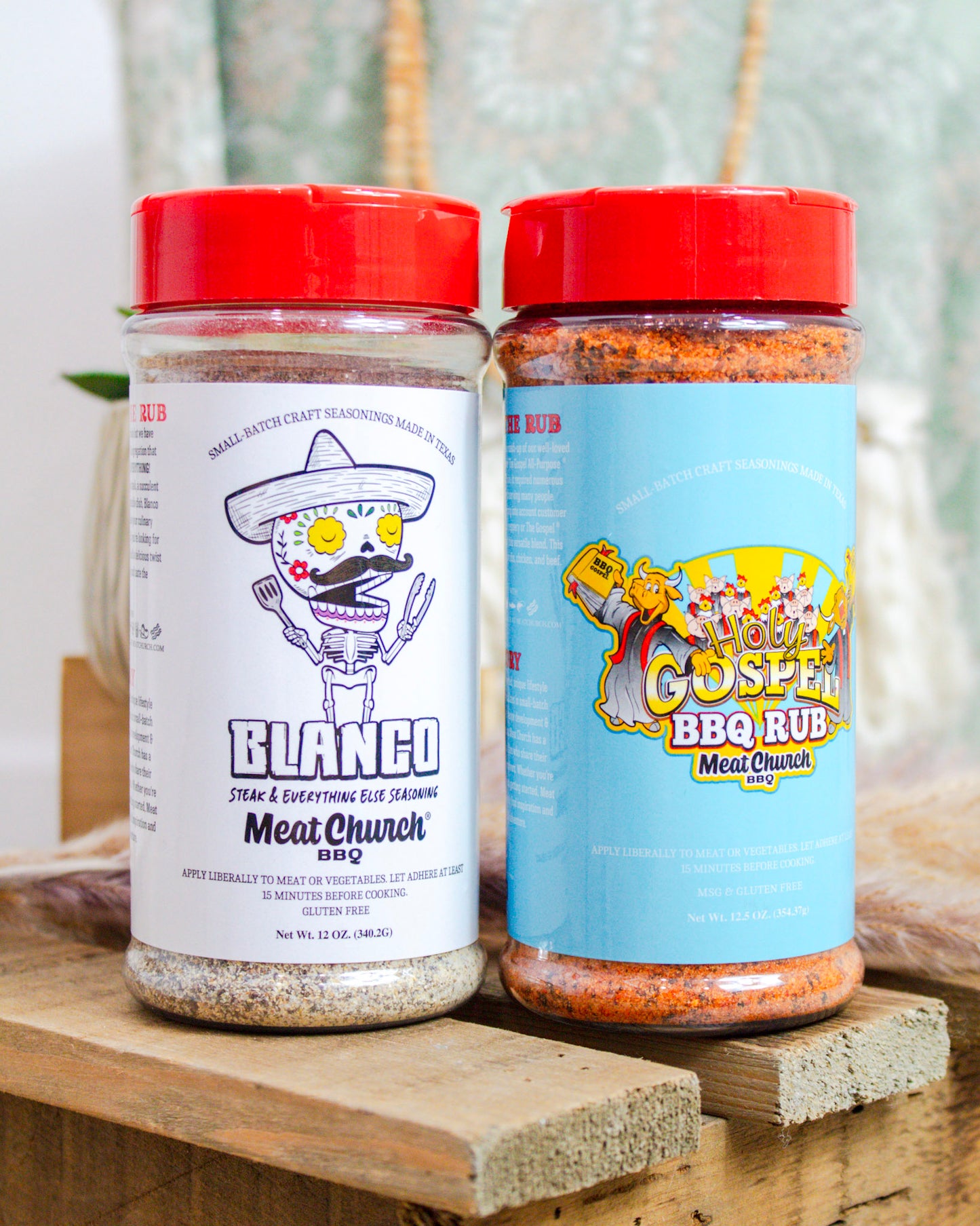Two jars of 'Meat Church' seasoning on a wooden surface with a blurred natural background