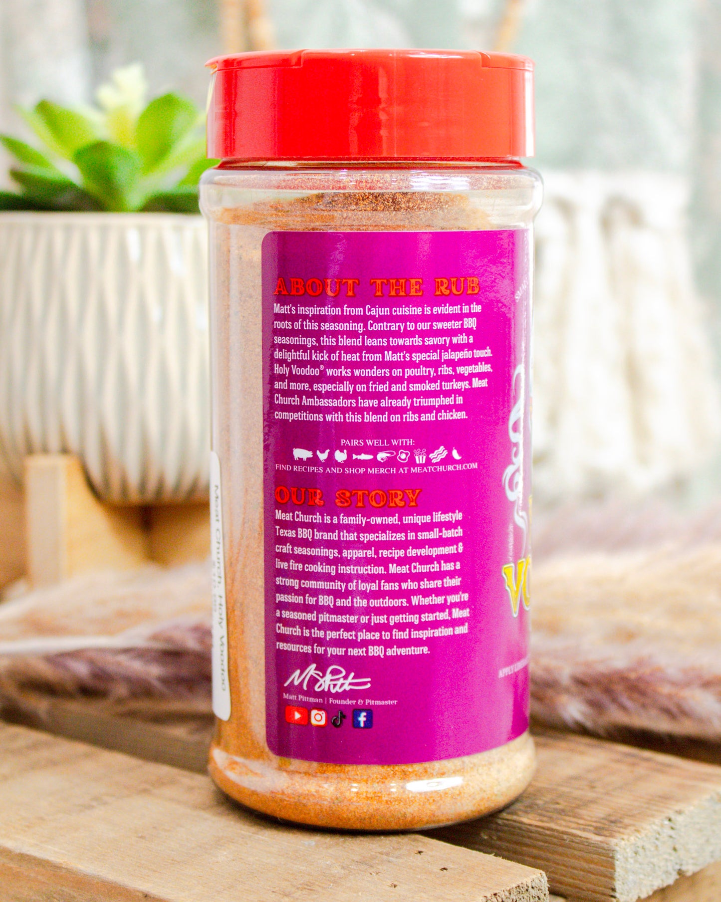 Bottle of seasoning with a red lid and purple label on a wooden surface.