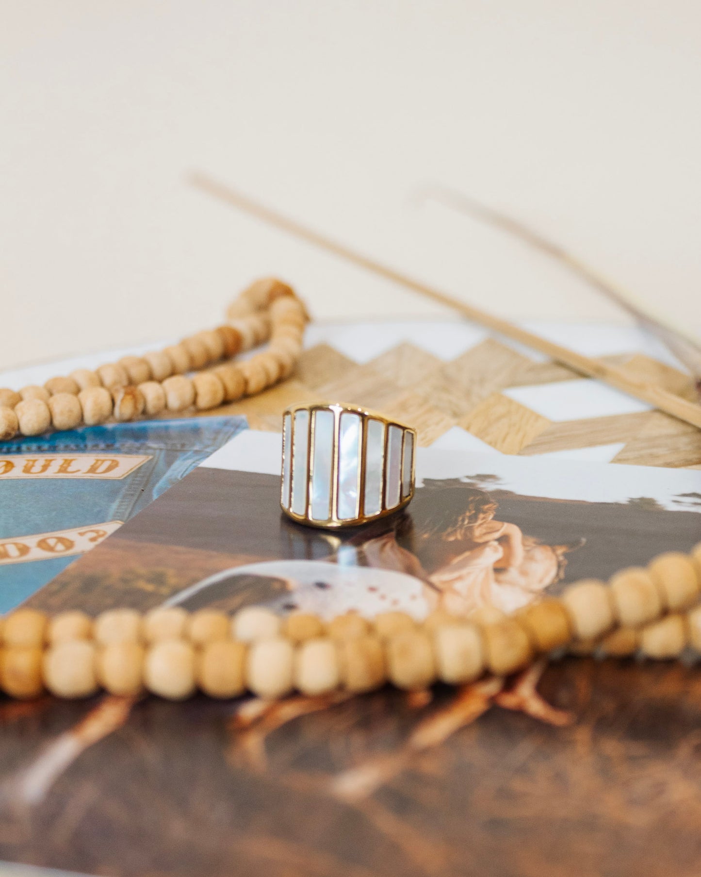 Gold statement ring with vertical mother-of-pearl inlays, displayed on natural wooden beads and a western-themed background