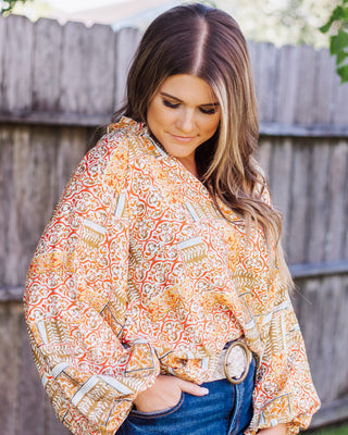 A woman models a bohemian-print balloon sleeve top with a ruffled neckline and belted waist.