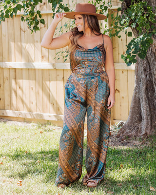 Woman wearing a boho-chic wide leg paisley pants in teal and gold tones, styled with a brown wide-brim hat and sandals for a relaxed outdoor look.