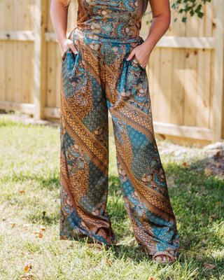 Close-up of women’s wide leg paisley print pants in teal and gold with side pockets, styled outdoors for a chic and relaxed boho look.