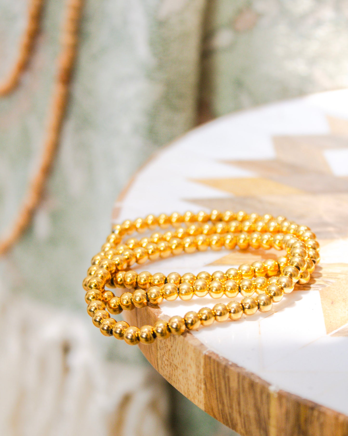 Set of gold beaded stretch bracelets displayed on a boho wood-and-resin side table in natural light.