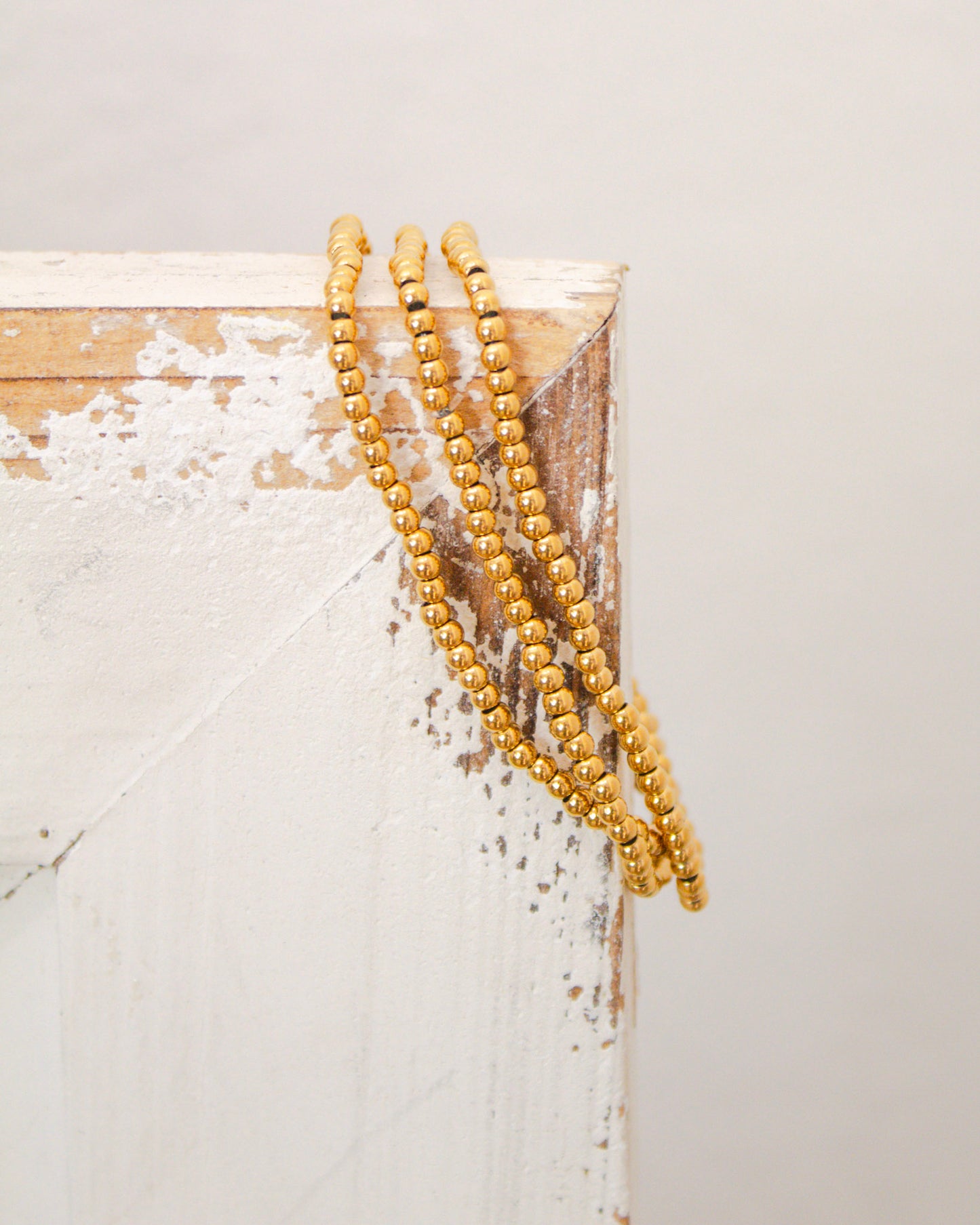 Set of gold beaded stretch bracelets draped over a distressed white wooden frame for a rustic display.