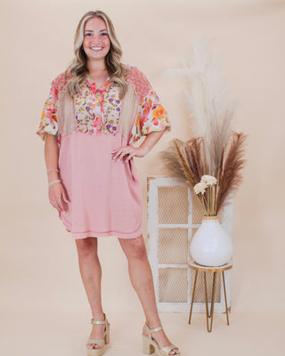 Smiling woman wearing a boho floral and pink patchwork dress with short sleeves and frayed hem, styled with gold heels in a neutral boutique setting