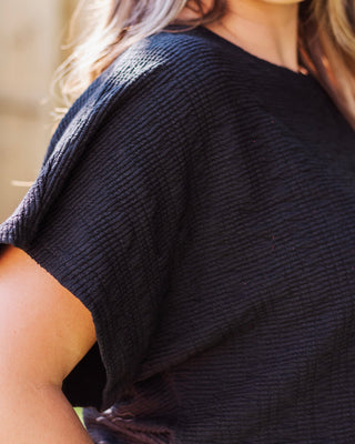 Close-up of a black textured fabric top, showing a waffle-knit or ribbed pattern.
