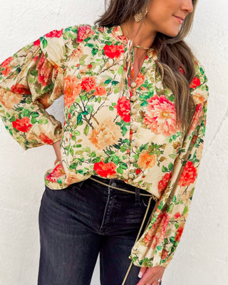 Floral satin blouse featuring a vintage-inspired rose print in red, peach, and green hues with button-down front and billowed sleeves—styled with dark jeans.