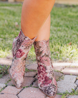 Close-up of women’s floral tapestry ankle boots with pointed toes and side zipper, styled outdoors on brick walkway for a chic western-inspired look.