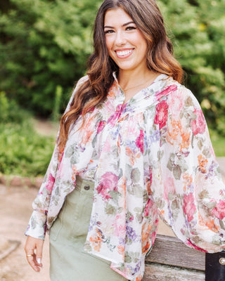 Woman wearing a lightweight floral blouse with watercolor-style prints in pink, orange, green, and lavender, styled with a sage green skirt for a chic spring outfit.