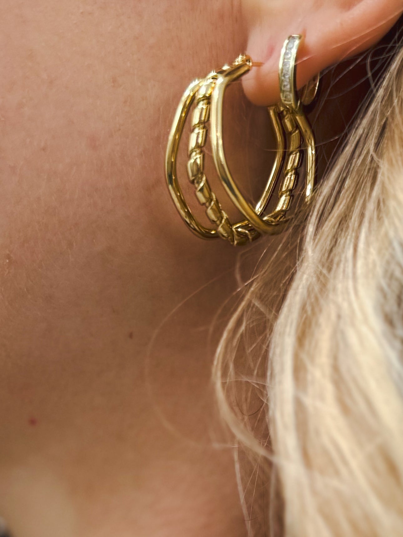 Close-up of a woman’s ear wearing three stackable gold hoop earrings in plain, chain-link, and braided textures, paired with a small diamond huggie stud