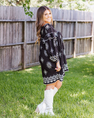 Black dress with white embroidery and ruffle details, styled with high white boots