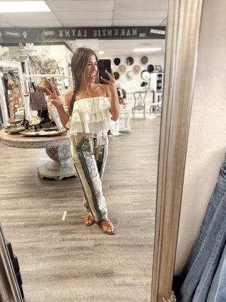 Woman taking mirror selfie in boutique wearing white ruffle strapless top and sage green patchwork pants—boho chic outfit from Makenzie Layne Boutique