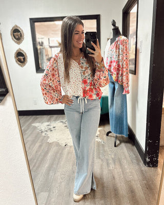Woman wearing a boho floral patchwork blouse with balloon sleeves and light wash flared jeans, styled for a chic boutique look inside MaKenzie Layne Boutique.