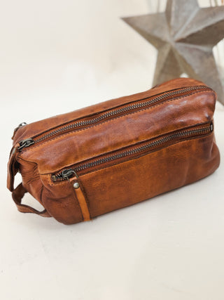 Handcrafted brown leather dopp kit with dual zipper compartments and handle, perfect for men's travel and grooming essentials.