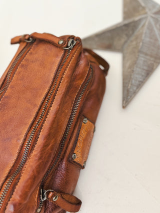 Close-up of handcrafted brown leather dopp kit with rugged zippers and branded patch, perfect for men’s travel and grooming essentials.