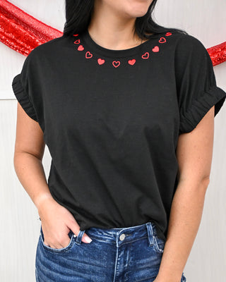 Black t-shirt with red heart patterns on a plain background
