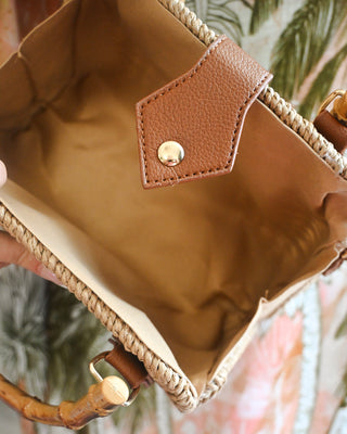 Interior view of a woven straw tote handbag with a spacious canvas-lined compartment, magnetic snap closure, vegan leather trim, and bamboo handles for chic summer boutique style.