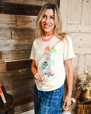 Women's ivory graphic tee featuring a colorful whimsical umbrella print, styled with blue plaid pants and a coral statement necklace for a playful boutique outfit.
