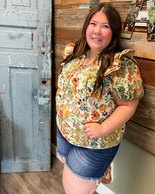 Curvy women’s colorful floral top with flutter sleeves and lightweight fabric, paired with dark wash denim shorts