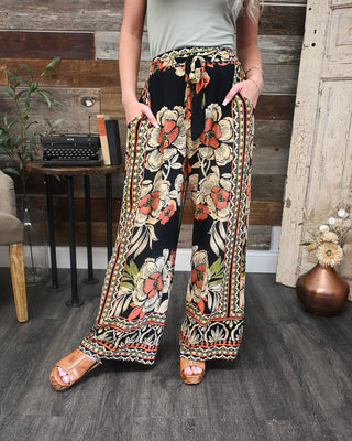 Women’s boho wide leg floral pants with a black base, coral and cream floral print, tie waist, and flowy fit perfect for vacation, brunch, and everyday boutique style.
