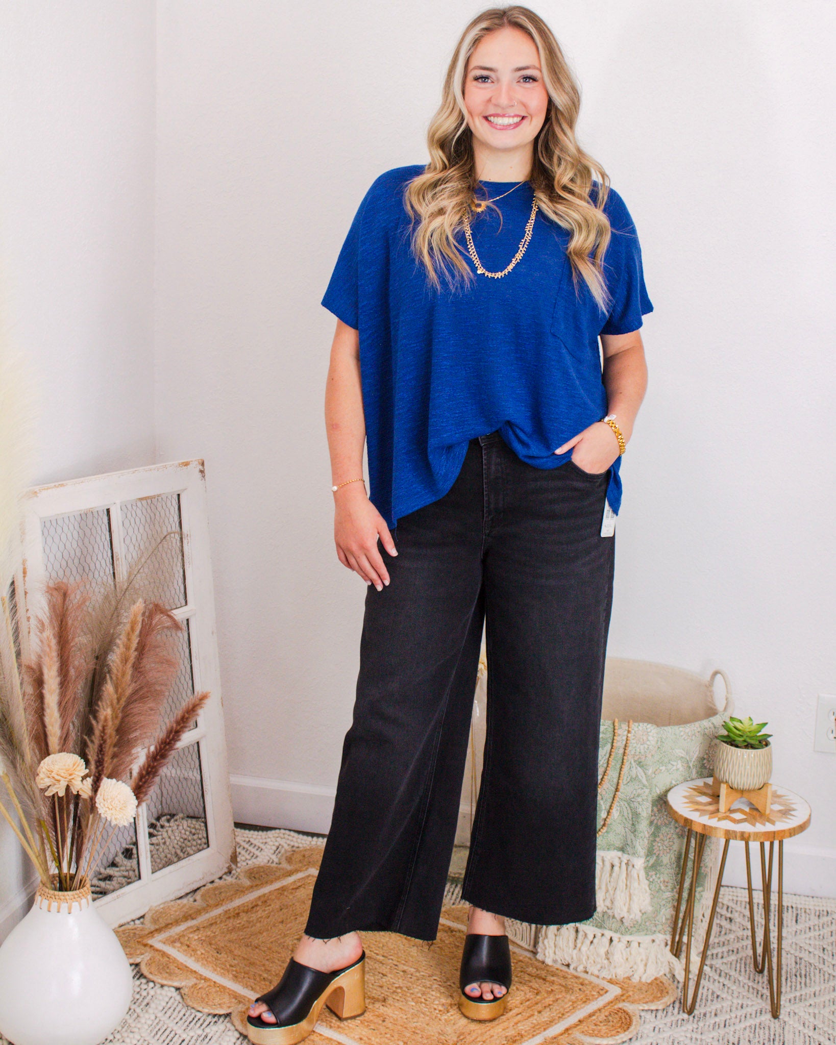 Woman wearing a cobalt blue short-sleeve top with black wide-leg jeans, gold jewelry, and platform heels.