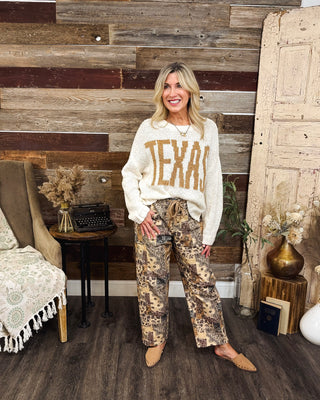 Women's ivory TEXAS graphic knit sweater with oversized tan lettering, styled with brown paisley patchwork wide-leg pants and tan flats for a trendy western-inspired fall outfit at MaKenzie Layne Boutique.
