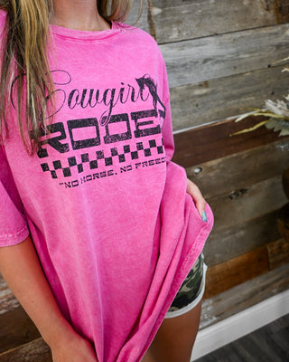 Hot pink “Cowgirl Rodeo” graphic tee with vintage wash, western slogan print, styled with camo denim shorts, casual boutique outfit with trendy oversized fit