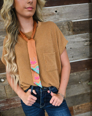 Women’s camel brown textured short sleeve top with chest pocket and relaxed fit, styled with dark wash jeans and a colorful western neck scarf.