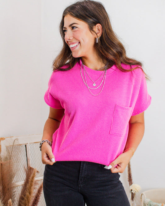 Woman wearing a hot pink textured short sleeve top with front pocket, paired with black jeans and layered silver necklaces, styled by MaKenzie Layne Boutique.