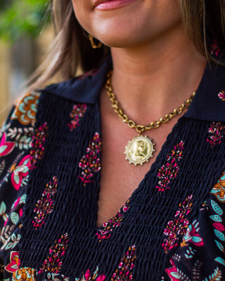 Close-up of a gold coin pendant necklace with a chunky chain, styled over a navy smocked floral blouse for a chic, boutique-inspired boho look.