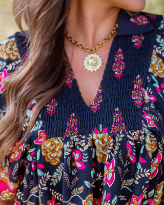 Close-up of a gold coin pendant necklace with a chunky chain, adding a bold vintage-inspired touch to a boho floral blouse outfit.