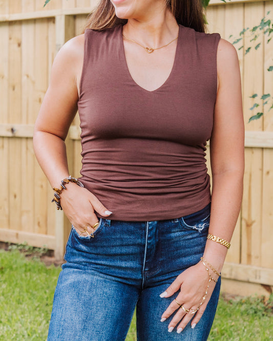 Close-up of woman wearing a sleeveless brown V-neck top paired with high-rise blue jeans and layered gold jewelry for a chic casual outfit.