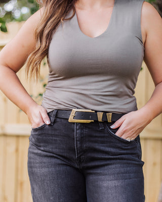 Woman wearing a taupe sleeveless top with a v-neckline tucked into high-waisted black jeans, styled with a bold black and gold belt for a chic neutral look.