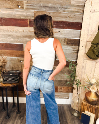 Back view of women’s high-rise light wash wide-leg jeans with patch pockets, styled with a fitted white tank for an effortless casual boutique look.