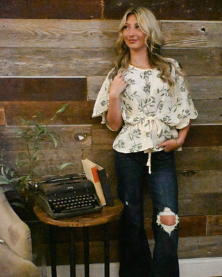 Cream floral print peplum blouse with flutter sleeves and adjustable tie waist paired with dark wash distressed flare jeans for chic boho boutique style.
