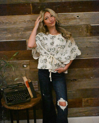 Cream floral print flutter sleeve blouse with front tie waist detail paired with dark wash distressed flare jeans for effortless boho boutique style and everyday wear.