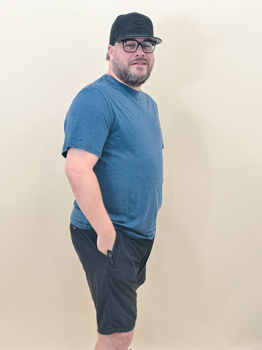 Man wearing a blue athletic crew neck t-shirt and black drawstring shorts, styled with a black Houston Astros cap and glasses for a casual sporty look.